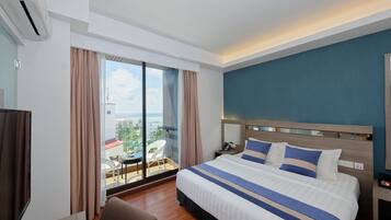 A hotel room with a large bed, a bedside table, a chair, and a view of the city through large windows.