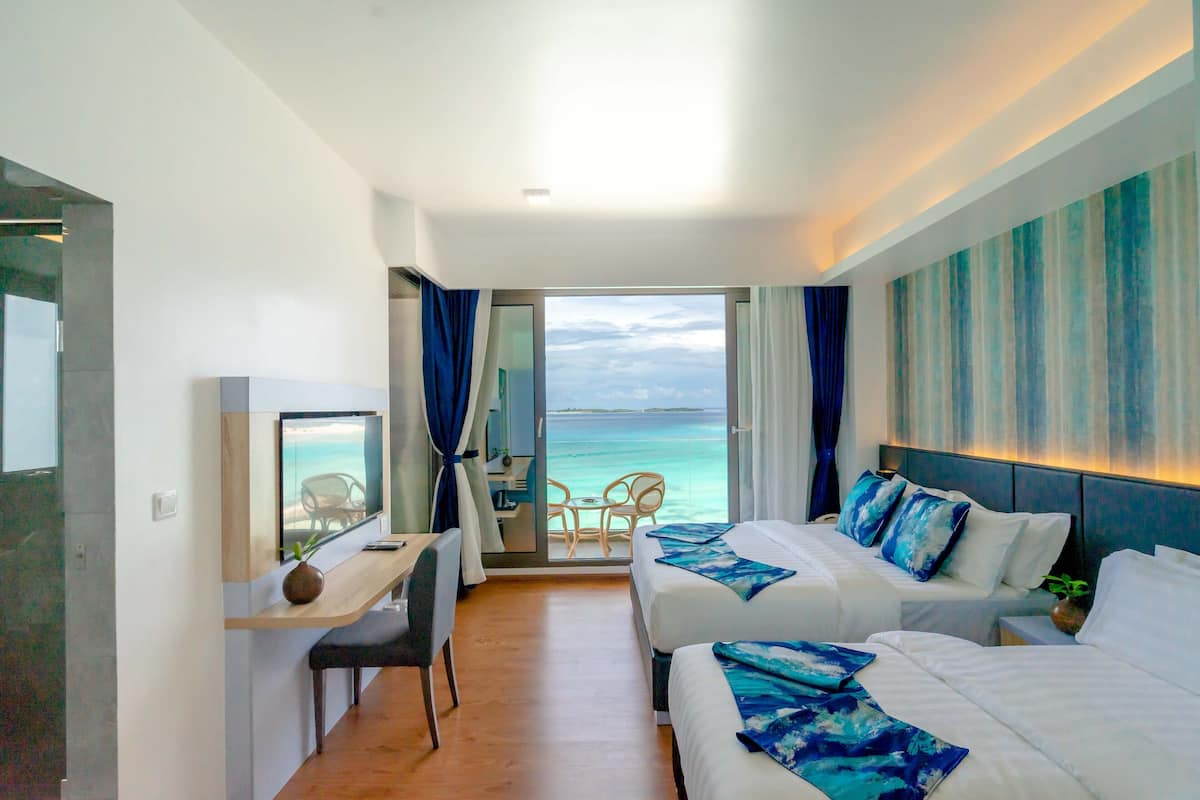 A hotel room with two beds, a desk, a chair, and a view of the ocean.