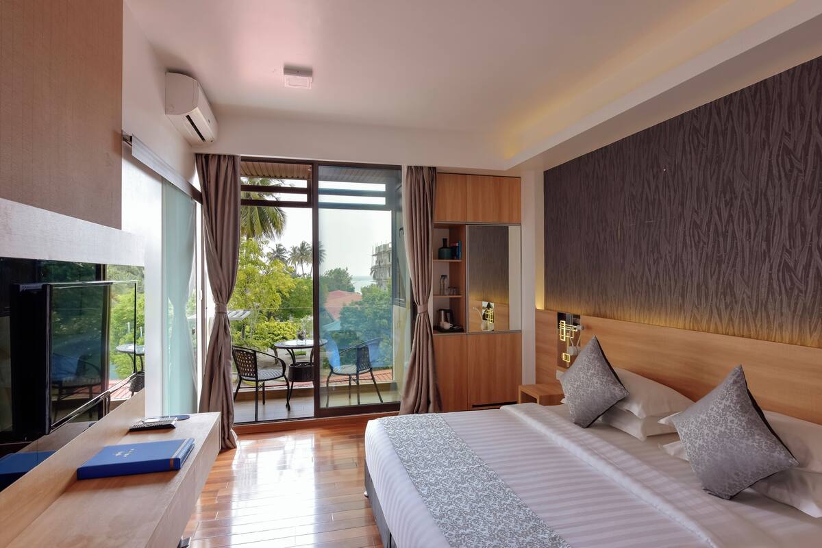 A modern hotel room with a large bed, a TV, and a balcony with a table and chairs.
