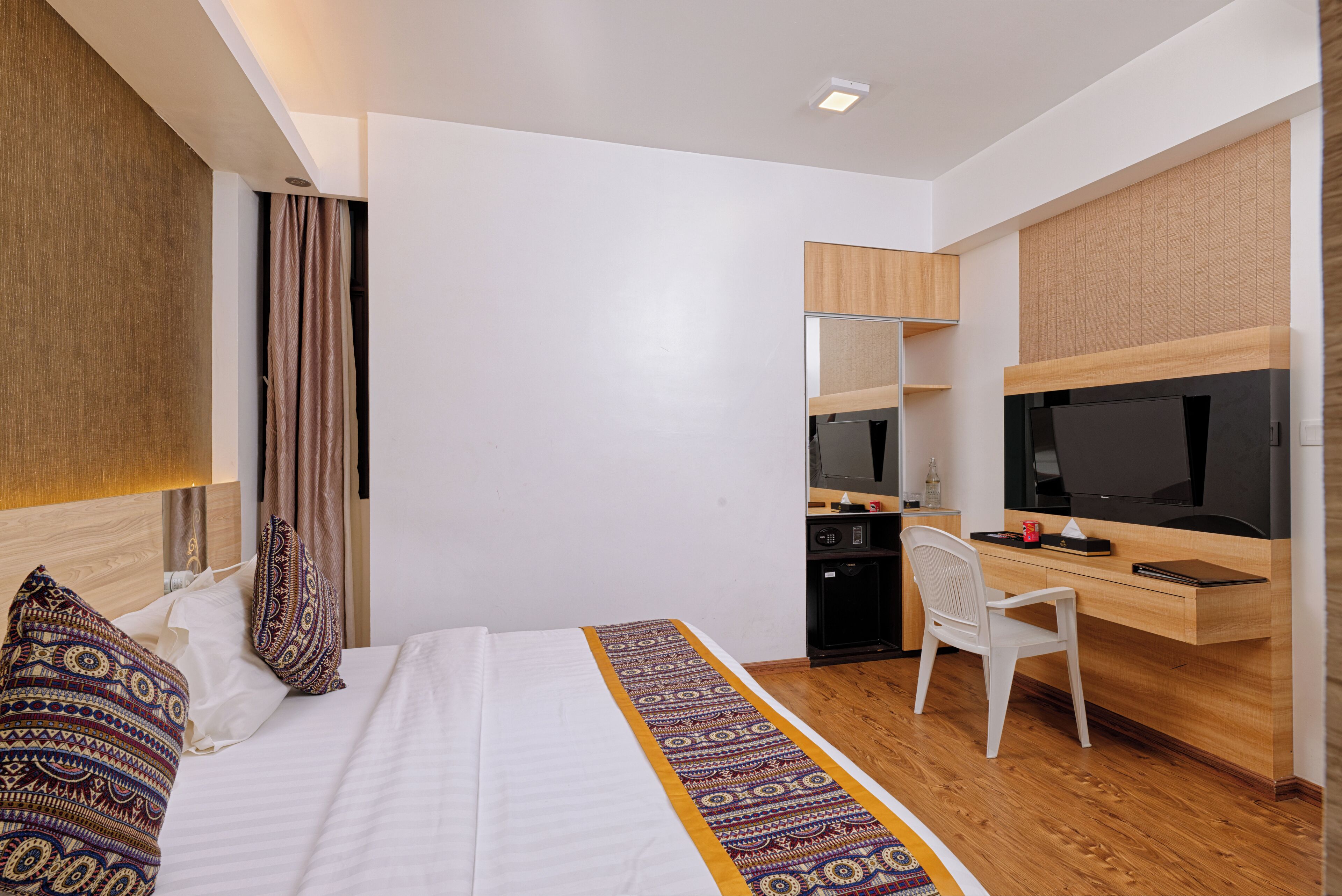 A modern hotel room with a bed, a desk with a computer, a television, and a wardrobe.