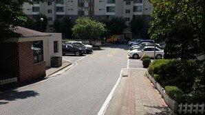 A parking lot with multiple cars, a small building on the left, and a row of trees and a fence on the right. - Spacious Apartment in Central Seoul (Seoul)