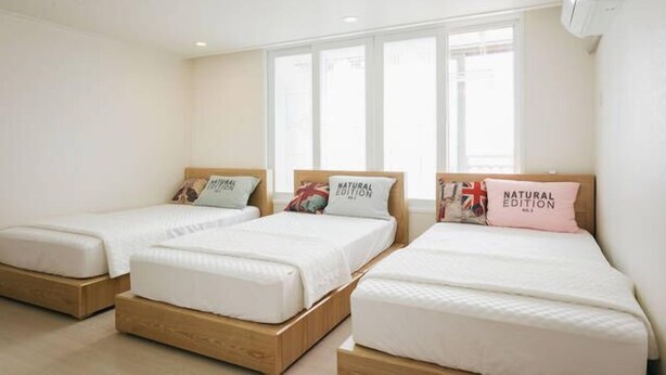 Three single beds with wooden frames and white bedding, arranged in a row with a large window behind them. - Spacious Apartment in Central Seoul (Seoul)