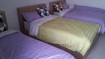 A room with two beds, each with a wooden headboard, purple bedding, and a variety of patterned pillows.