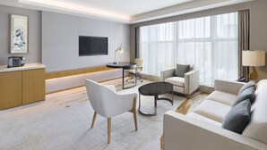 A modern hotel room with a sofa, armchair, and a small table. There is a TV mounted on the wall and a window with curtains. - Courtyard by Marriott Zhengzhou East (Zhengzhou)