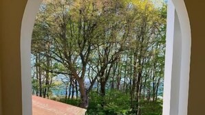 Une vue depuis une fenêtre à cadre blanc, donnant sur un espace pavé avec des arbres et un bâtiment doté d’un toit rouge.