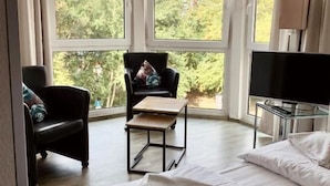 Une chambre d’hôtel avec une grande fenêtre, un lit, une chaise, une petite table et un téléviseur.