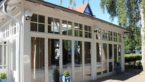 Un espace extérieur abrité, doté de grandes fenêtres en verre et d’une façade blanche.