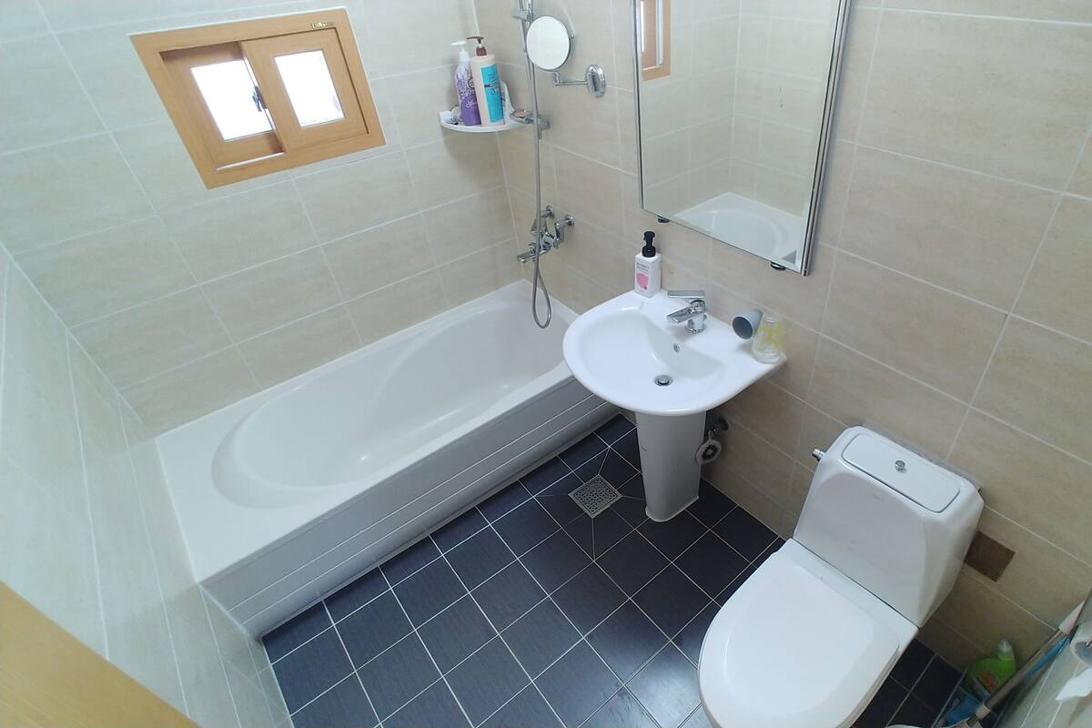 A bathroom with a bathtub, sink, toilet, and a small window.