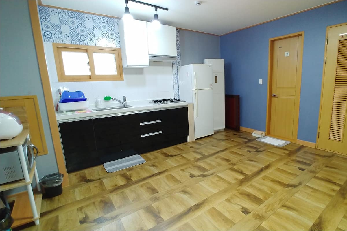 A kitchen with a tiled backsplash, a sink, a stove, and a refrigerator. There are wooden cabinets and a door with a window.