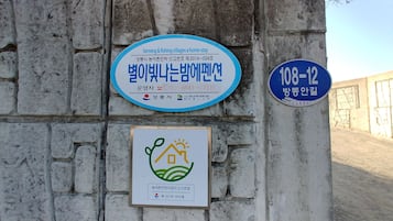 A wall with three signs: a blue sign with Korean text, a blue circular sign with numbers, and a white sign with a green and yellow logo.