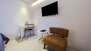 A small, modern room with a white desk, a chair, a television mounted on the wall, and a small side table with a remote control. - Hotel Myeongjak (Chuncheon)