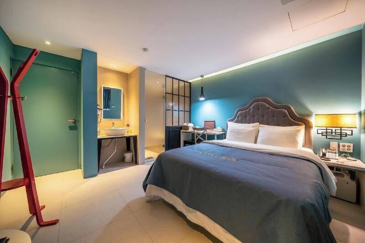 A hotel room with a bed, bedside table, lamp, and a desk with a chair.