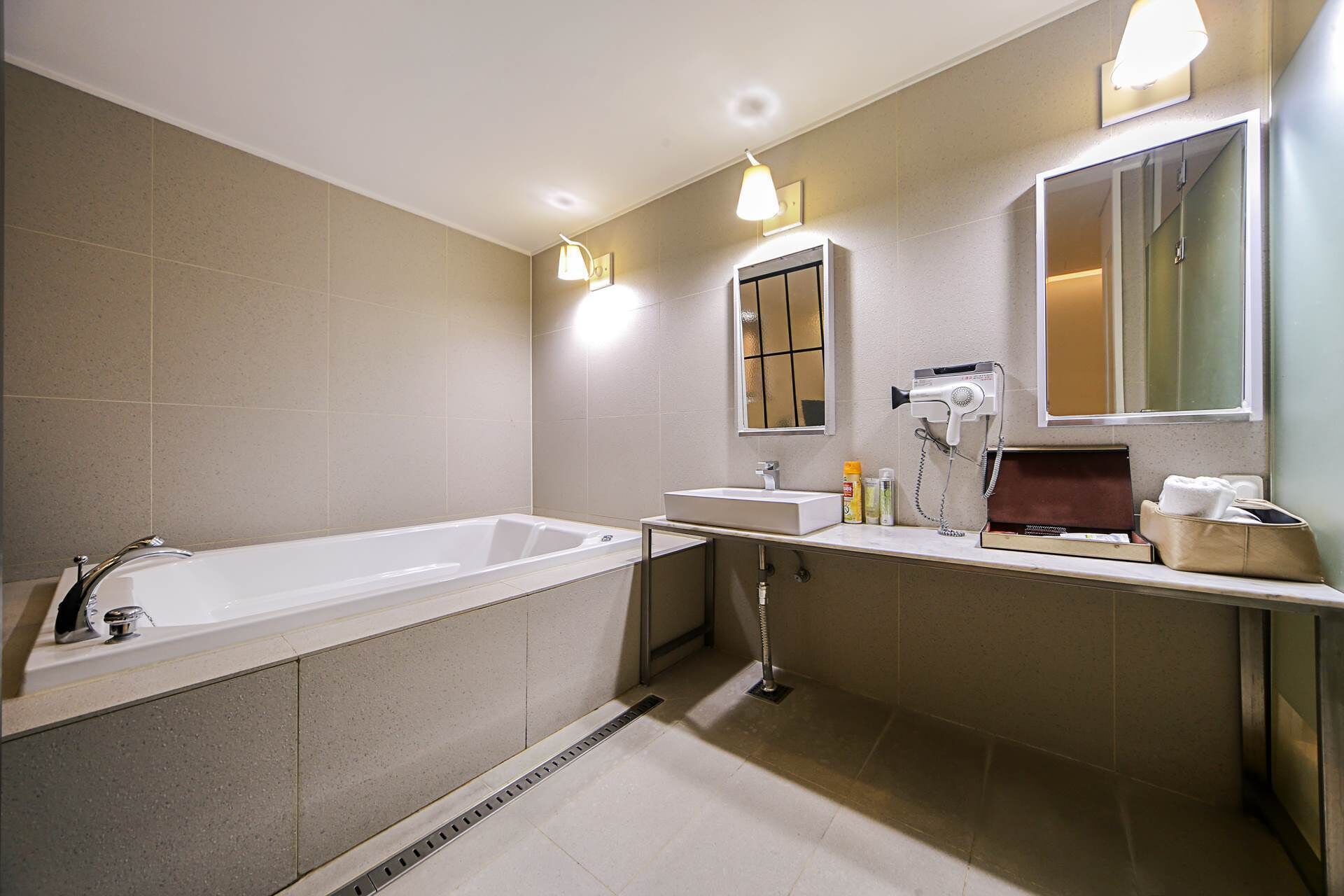 Un baño moderno con una bañera grande, un lavabo y un espejo. Hay luces en el techo y un secador de pelo en la encimera.