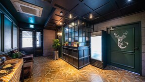 A modern interior with a patterned floor, a reception desk, a door with a deer logo, and a window with natural light. - Hotel Myeongjak (Chuncheon)
