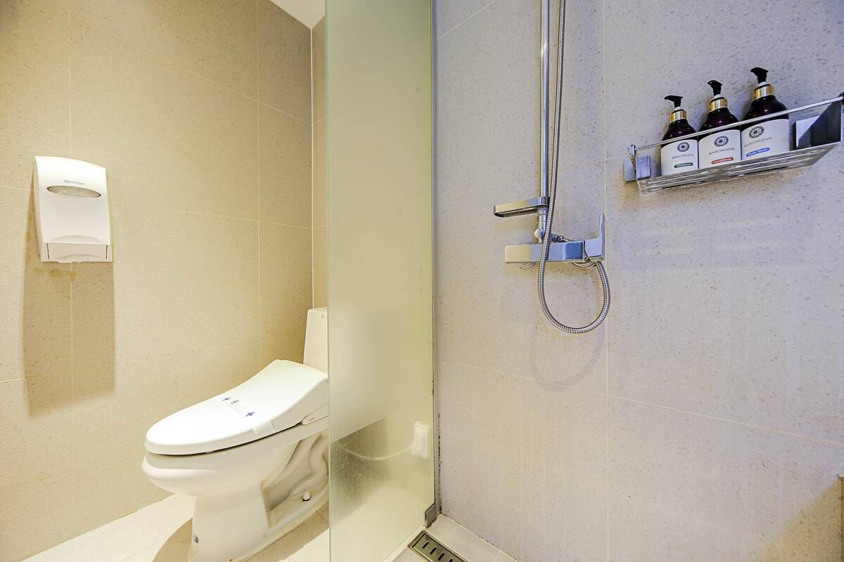A modern bathroom with a toilet, a glass-enclosed shower, and a shelf with toiletries.