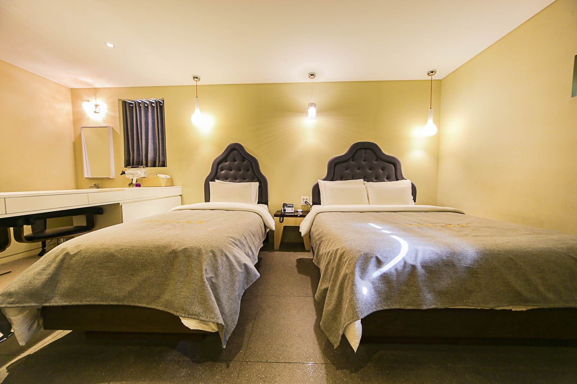 A hotel room with two beds, a desk, and a mirror.