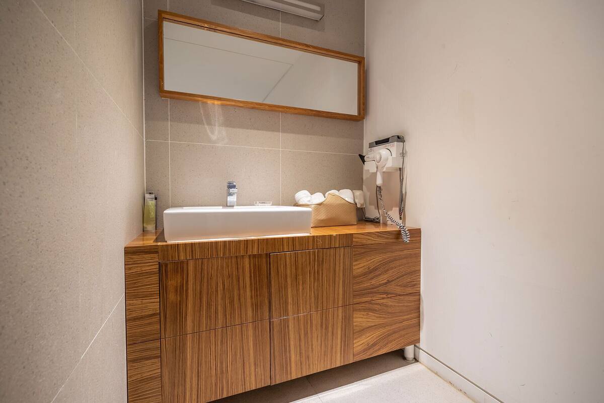 A bathroom with a wooden vanity, a white sink, a mirror, and a hairdryer.