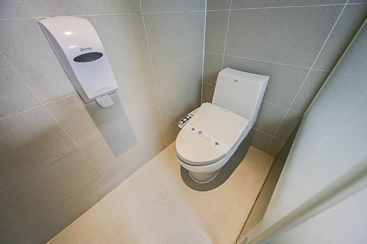 A modern bathroom with a toilet, a hand dryer, and a toilet paper dispenser.