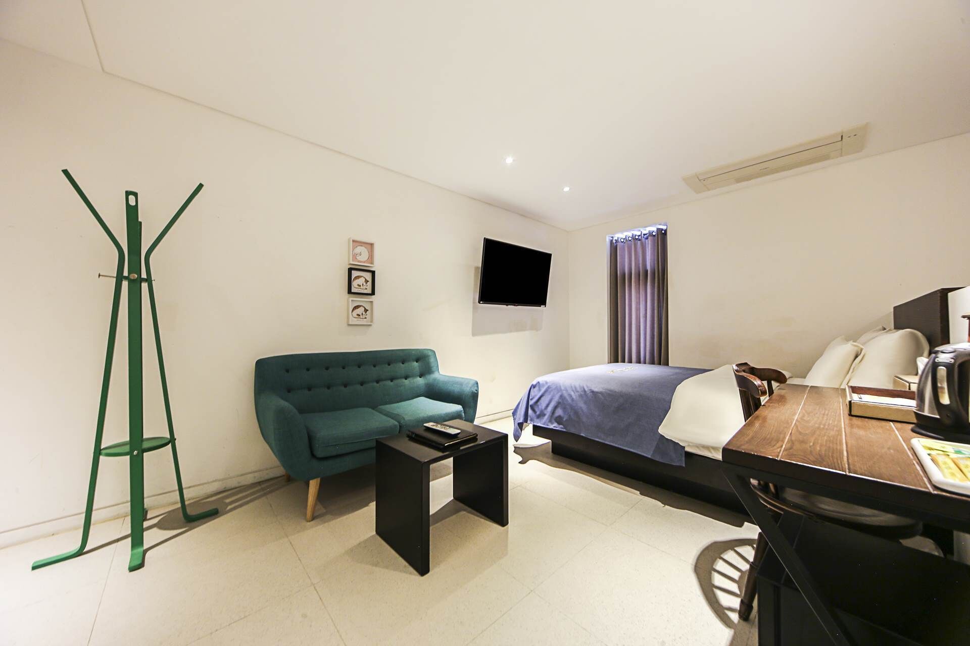 A compact hotel room with a bed, a green sofa, a small table, a TV, and a window with curtains.