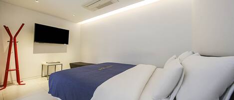 A modern hotel room with a bed, a flat-screen TV, a desk, and a red chair.