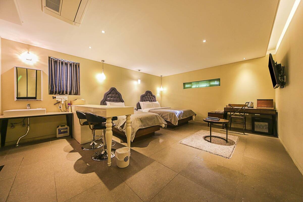 A compact hotel room with two beds, a desk, a chair, a small table, and a television.