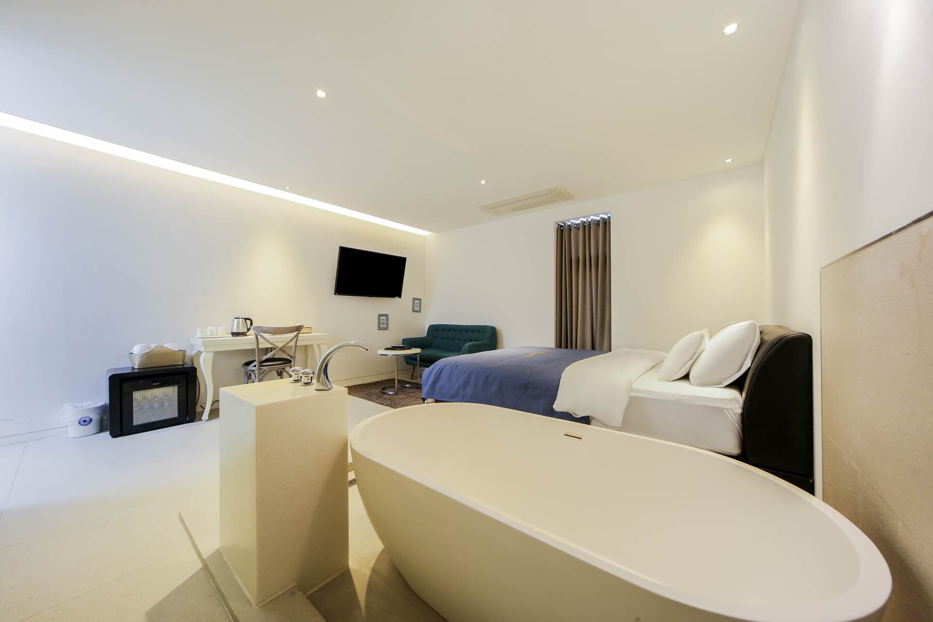 Une chambre d’hôtel moderne dotée d’une grande baignoire, d’un téléviseur à écran plat fixé au mur, d’un bureau avec une chaise et d’un canapé.
