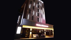 A multi-story building with a brightly lit ground floor, possibly a hotel or commercial establishment, featuring a large sign and several parked cars. - Hotel Myeongjak (Chuncheon)