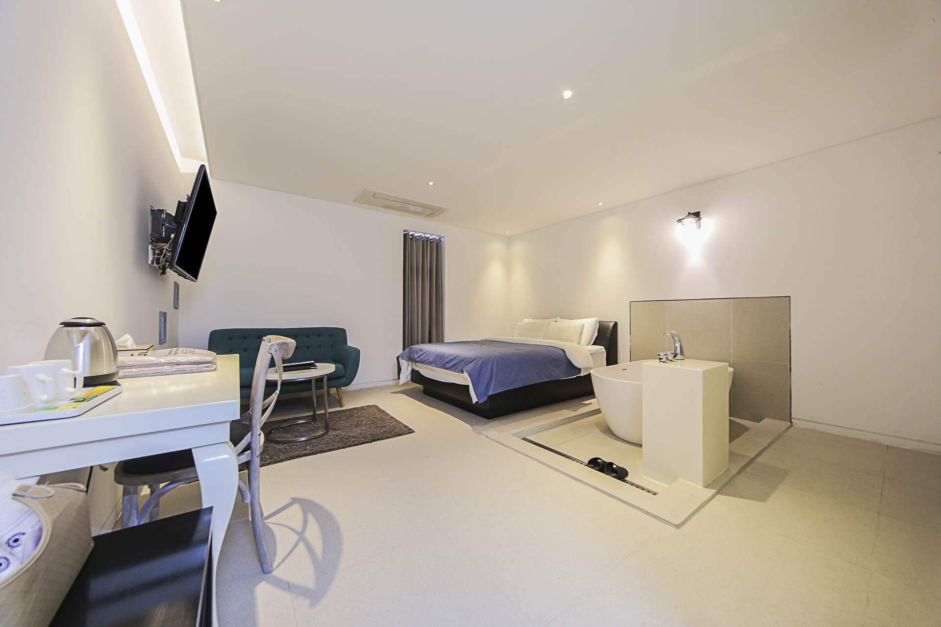 A modern hotel room with a bed, bedside table, and a desk with a chair.