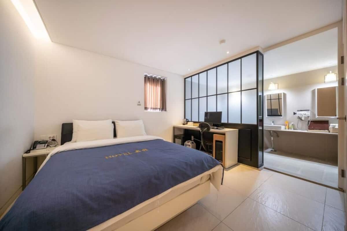 A hotel room with a bed, desk, computer, and a bathroom.