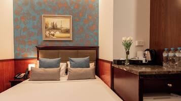 Habitación de hotel con cama, mesita de noche con teléfono, un cuadro en la pared y una pequeña mesa con un jarrón de flores.