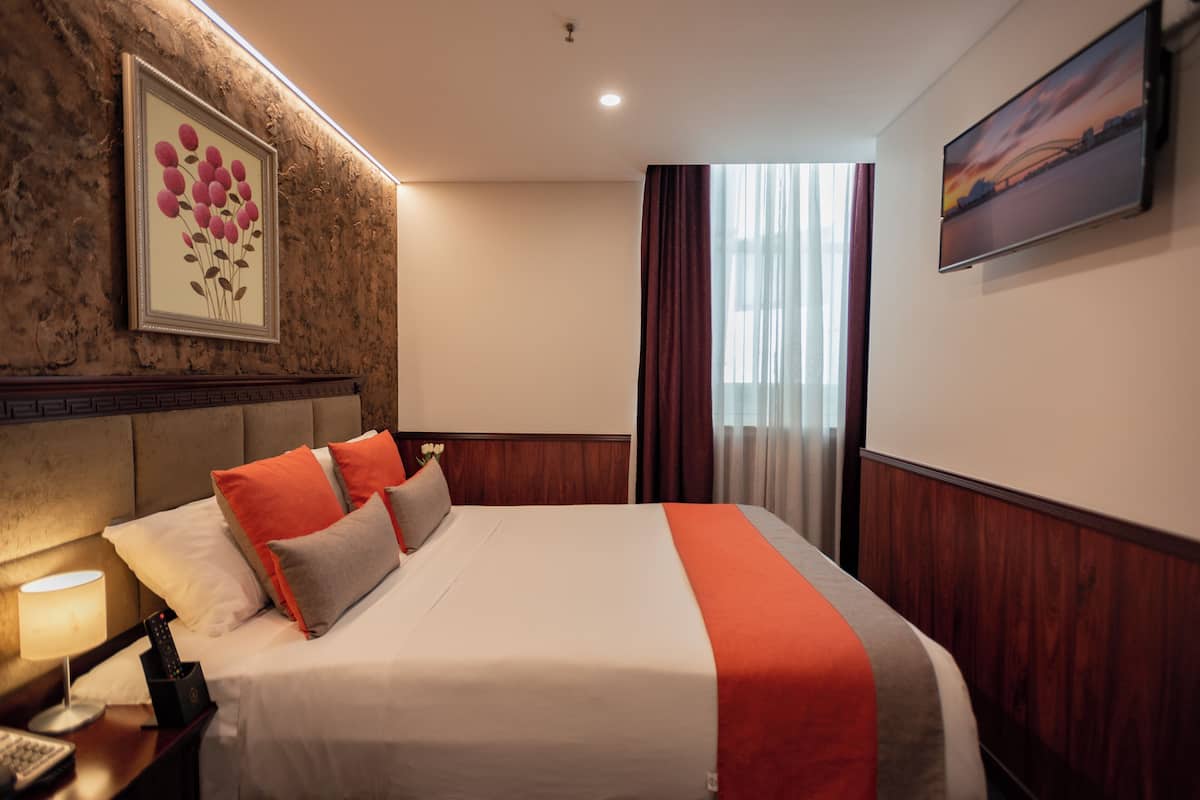 A hotel room with a large bed, a nightstand with a lamp, a framed floral artwork on the wall, and a painting above the bed.