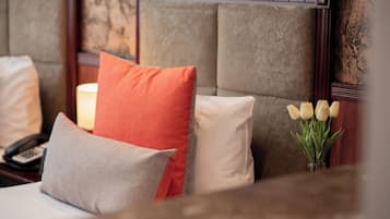 Una habitación de hotel con cama, almohadas, lámpara de noche, teléfono y un jarrón con flores.