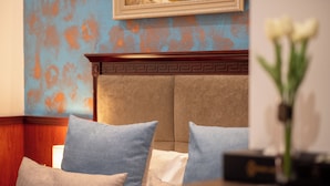 Una habitación de hotel con cama, almohadas, un florero con flores y un cuadro en la pared.
