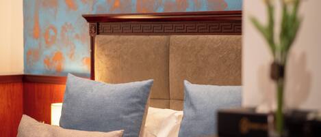 Una habitación de hotel con cama, almohadas, un florero con flores y un cuadro en la pared.