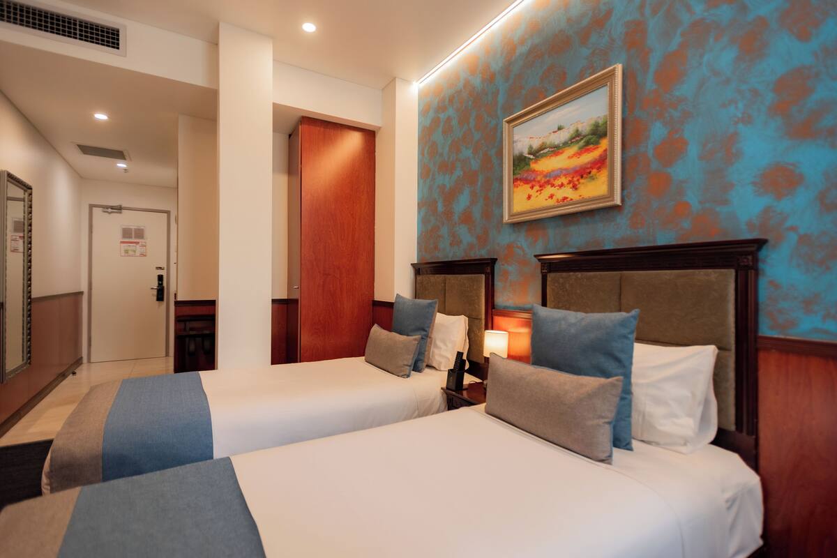 A hotel room with two beds, a painting on the wall, and a wooden headboard.