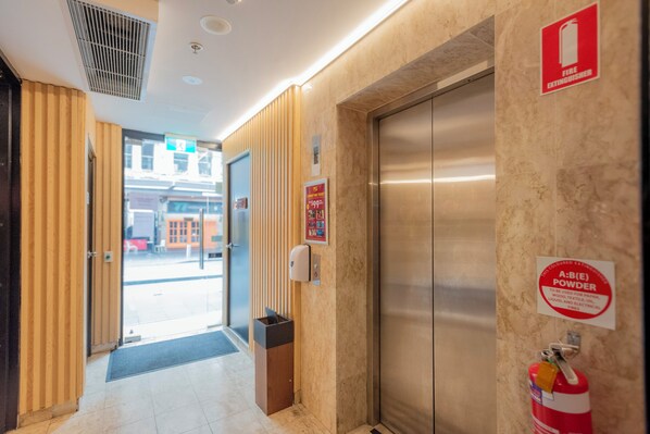 A hotel lobby with a reception desk, a fire extinguisher, and an elevator.