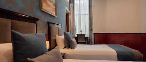 Quarto de hotel com duas camas, um quadro na parede e uma janela com cortinas.
