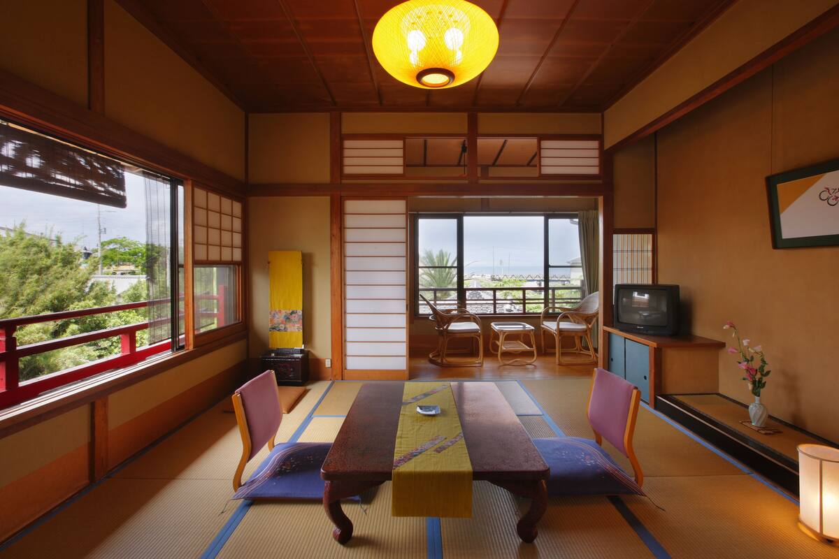 A traditional Japanese room with tatami flooring, a low table, and a television on a cabinet.