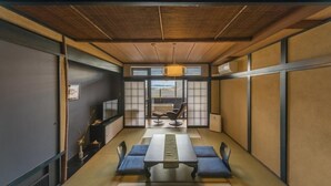 A traditional Japanese-style room with tatami flooring, a low table with cushions, a sliding door leading to a balcony, and a hanging light fixture. - Chikurakan (Minamiboso)
