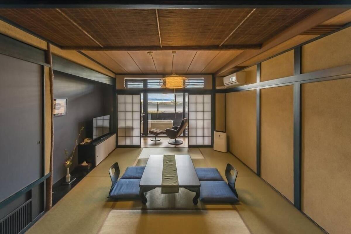 A traditional Japanese-style room with tatami flooring, a low table with cushions, a sliding door leading to a balcony, and a hanging light fixture.