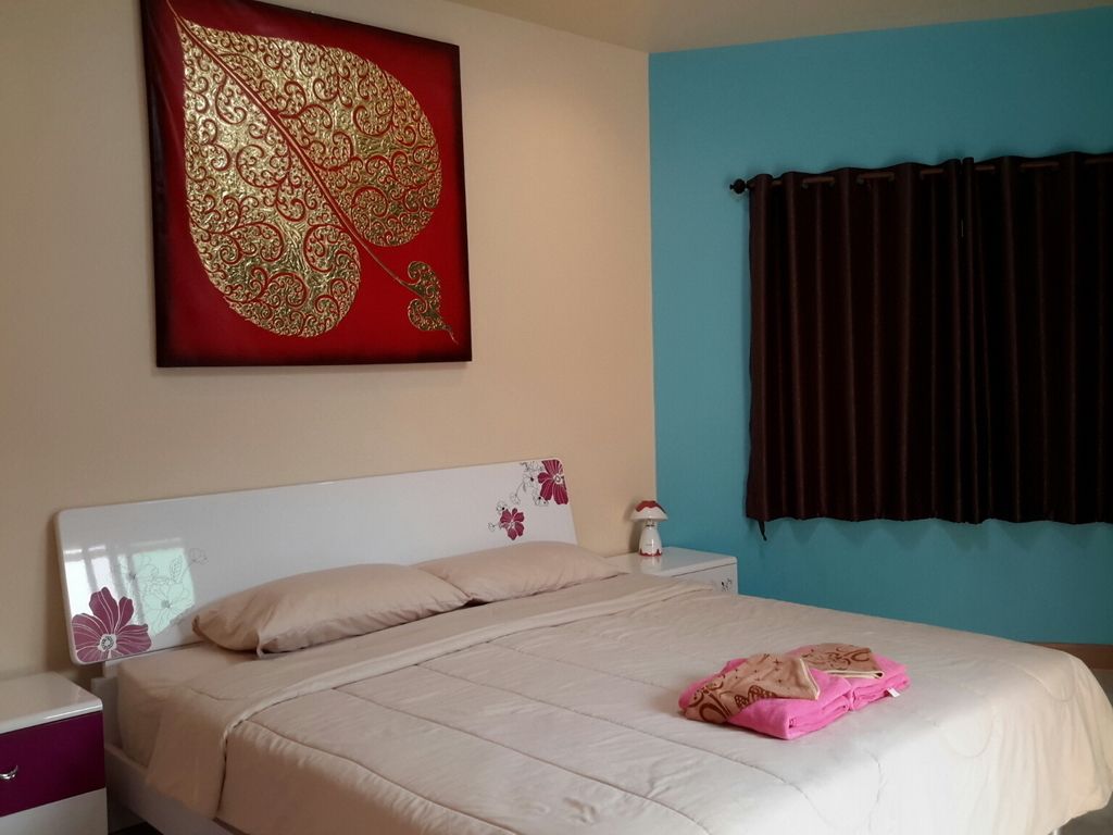 Un dormitorio con cama, mesita de noche, lámpara, un gran adorno en la pared y una ventana con cortinas.