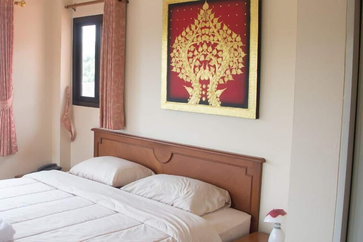 A neatly made bed with white linens and a wooden headboard, a window with curtains, and a framed artwork on the wall.