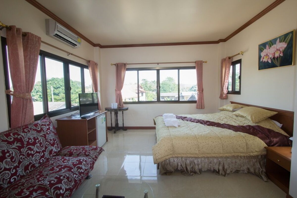 A bedroom with a bed, a sofa, a desk with a television, and large windows.