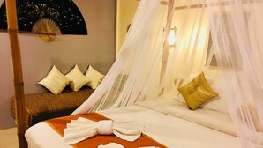 A four-poster bed with white linens and a brown bedspread, a canopy, and a wall-mounted fan.