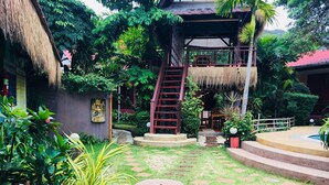 A tropical garden with a thatched-roof structure, a wooden staircase, and a small pool area.