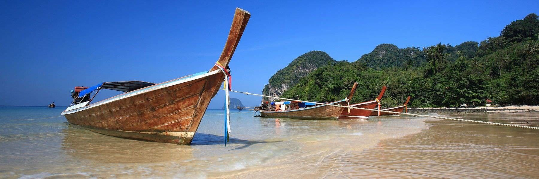 A row of traditional wooden boats anchored on a clear beach with a backdrop of lush green hills.