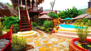 A tropical resort with a swimming pool, a wooden staircase, and thatched-roof structures.