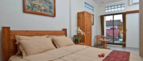 Un dormitorio con una cama grande, cabecera de madera, ventilador de techo, armario de madera, una mesita con una silla y una ventana con vistas al exterior.