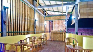 A wooden deck with tables and chairs, bamboo walls, and a bar area. - Kuta EcoStay (Kuta)