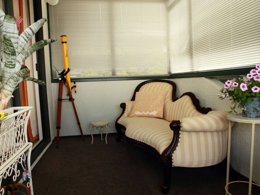 A corner room with a dark wooden sofa, a tripod, and a small stool.